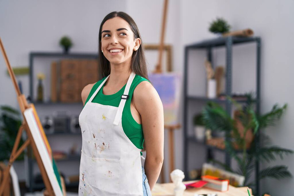 Молодая латиноамериканка-художница улыбается уверенно стоя на арт-студии - Фото, изображение