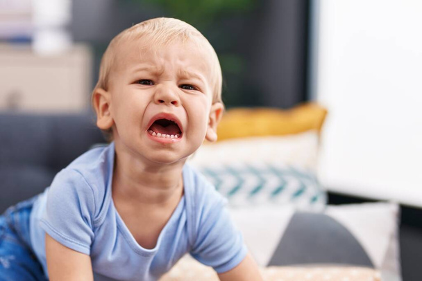 Adorable toddler sitting on sofa crying at home - Photo, image