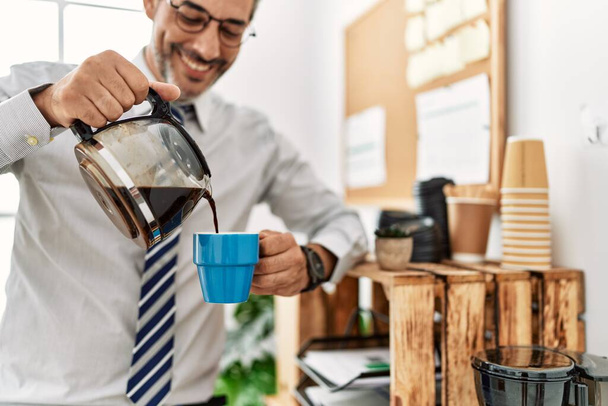 Седовласый бизнесмен средних лет наливает кофе на чашку в офисе - Фото, изображение