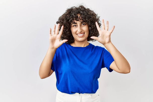 Ortadoğulu genç bir kadın izole edilmiş arka planda duruyor ve 10 numaralı parmaklarıyla işaret ederken kendinden emin ve mutlu bir şekilde gülümsüyor..  - Fotoğraf, Görsel
