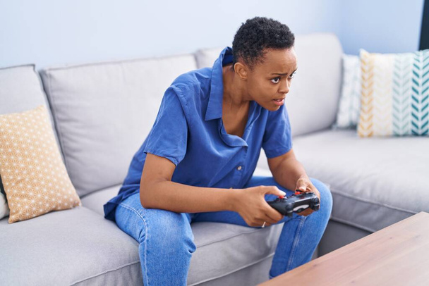 Африканська американка грає у відеоігри, сидячи вдома на дивані. - Фото, зображення
