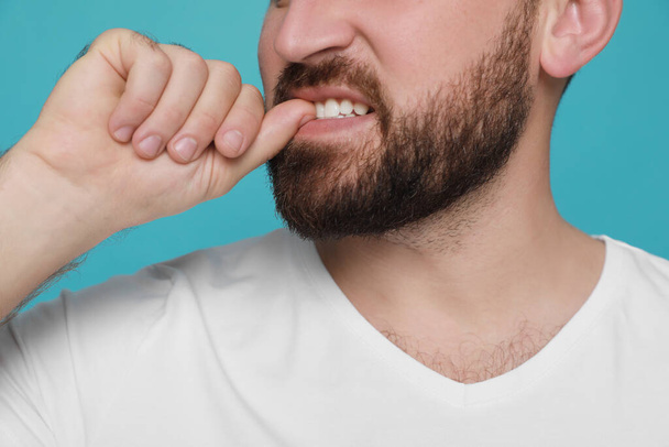Man biting his nails on light blue background, closeup. Bad habit - Φωτογραφία, εικόνα