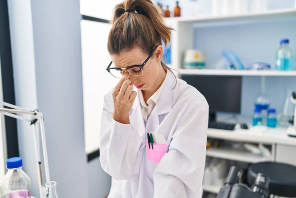 Young woman wearing scientist uniform stressed working at laboratory - Foto, imagen