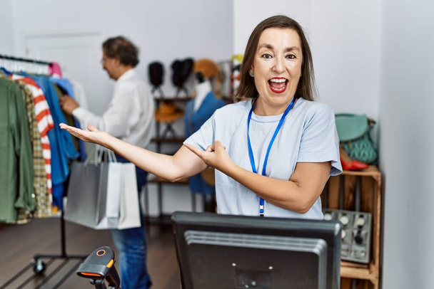 Mulher hispânica de meia-idade trabalhando como gerente na loja de varejo espantado e sorrindo para a câmera enquanto se apresenta com a mão e apontando com o dedo.  - Foto, Imagem