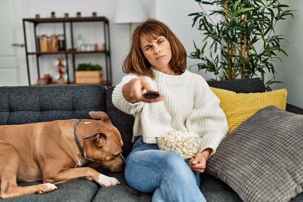 Jovem caucasiana assistindo filme sentado no sofá com o cão em casa - Foto, Imagem