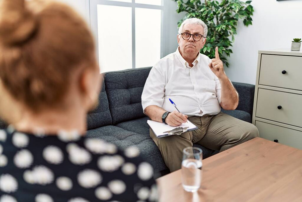 Senior-Psychologe Mann in der Beratungsstelle zeigt nach oben Blick traurig und aufgebracht, zeigt Richtung mit den Fingern, unglücklich und deprimiert.  - Foto, Bild