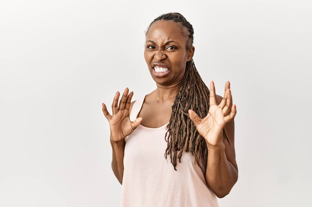 Schwarze Frau mit Zöpfen, die über isoliertem Hintergrund steht angewidert Ausdruck, unzufrieden und ängstlich dabei Ekel Gesicht, weil Abneigung Reaktion. mit erhobenen Händen  - Foto, Bild
