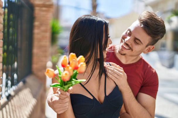 Man and woman couple hugging each other holding bouquet of flowers at street - Photo, Image