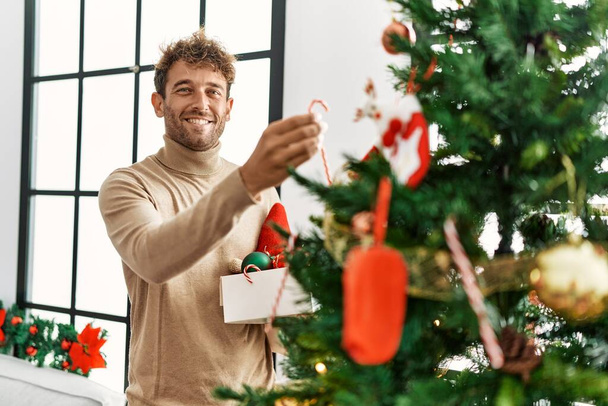 Jeune homme hispanique souriant décoration confiante arbre de Noël à la maison - Photo, image