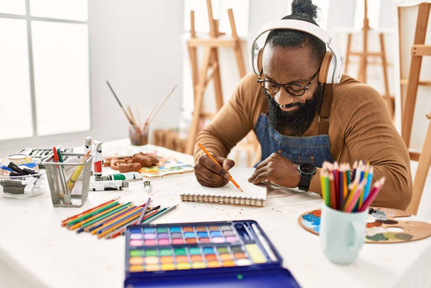 Young african american artist man using headphones drawing at art studio. - Zdjęcie, obraz