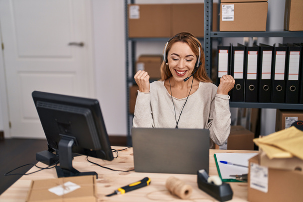 Hispanic woman working at small business ecommerce wearing headset screaming proud, celebrating victory and success very excited with raised arms  - Foto, Imagen