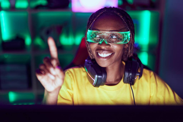 Streamer mujer afroamericana jugando videojuegos usando gafas de realidad virtual en la sala de juegos - Foto, imagen