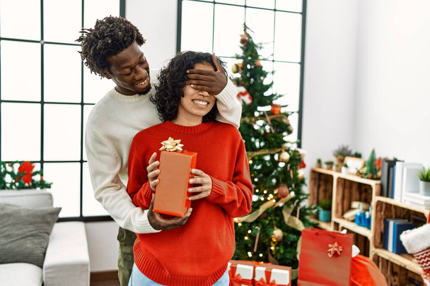 Young african american man surprisng his girlfriend with christmas gift at home. - Photo, Image