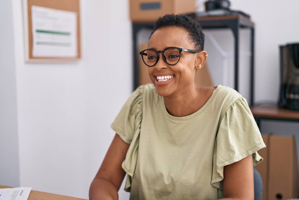 African american woman business worker smiling confident sitting on table at office - Foto, afbeelding