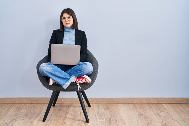 Mujer hispana joven sentada en silla usando computadora portátil deprimida y preocupada por la angustia, llorando enojada y asustada. expresión triste.  - Foto, Imagen