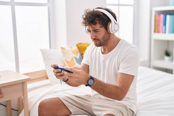 Junger hispanischer Mann spielt Videospiel auf Bett im Schlafzimmer - Foto, Bild