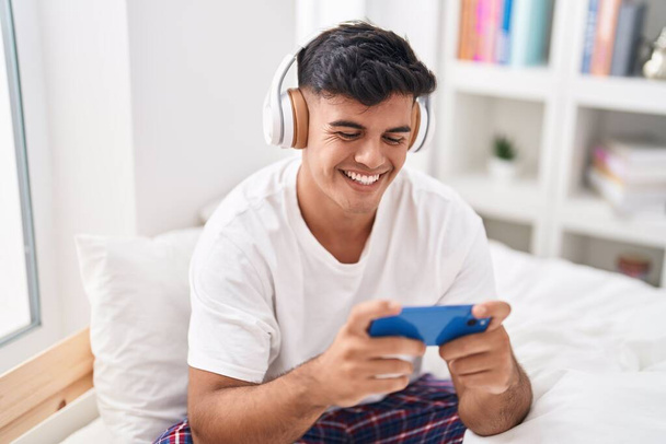 Giovane uomo ispanico sorridente fiducioso giocare al videogioco in camera da letto - Foto, immagini