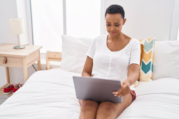 African american woman using laptop sitting on bed at bedroom - Foto, Imagem