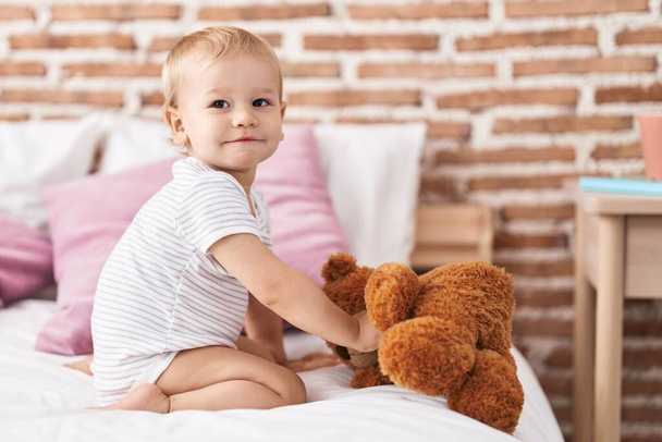 Adorável criança brincando com ursinho sentado na cama no quarto - Foto, Imagem
