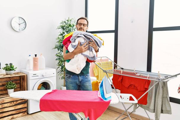 Uomo ispanico di mezza età che fa lavori domestici tenendo i vestiti a casa. - Foto, immagini