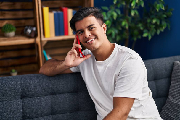 Giovane uomo ispanico che parla sullo smartphone seduto sul divano di casa - Foto, immagini
