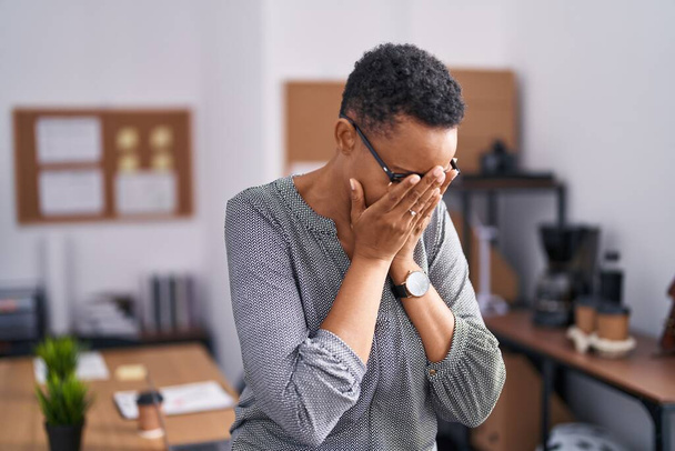 Femme afro-américaine travaillant au bureau portant des lunettes avec une expression triste couvrant le visage avec les mains tout en pleurant. concept de dépression.  - Photo, image