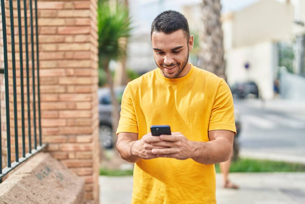 Молодой латиноамериканец уверенно улыбается, используя смартфон на улице - Фото, изображение