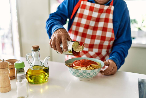 Senior man gieten tomatensaus op spaghetti in de keuken - Foto, afbeelding
