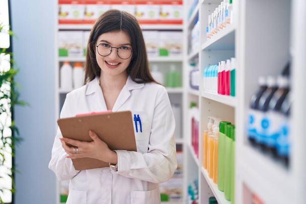 Joven mujer caucásica farmacéutico escribiendo en el documento en la farmacia - Foto, imagen
