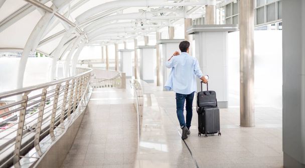 A visão traseira de um homem segurando uma xícara de café e puxando a bagagem enquanto ele está esperando por seu amigo no aeroporto. - Foto, Imagem