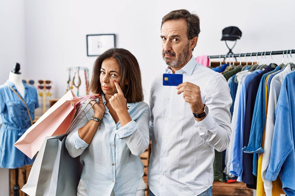 Alışveriş torbaları ve kredi kartı tutan İspanyol orta yaşlı bir çift jestini izlerken gözüne işaret ediyor. Şüpheli bir ifade.  - Fotoğraf, Görsel