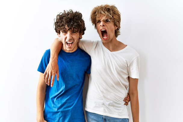 Young gay couple standing together over isolated background angry and mad screaming frustrated and furious, shouting with anger. rage and aggressive concept.  - Фото, зображення