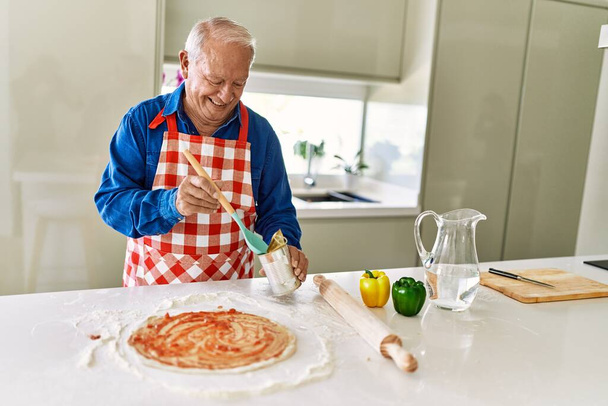 Старший чоловік посміхається впевнено готує піцу на кухні
 - Фото, зображення