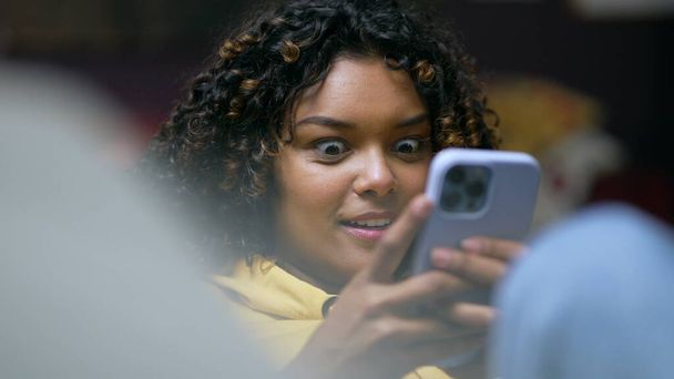 Szczęśliwy młody Afroamerykanin śmiejący się i uśmiechający podczas korzystania z telefonu w nocy. Osoba autentyczny spontaniczny prawdziwe życie śmiech i uśmiech - Zdjęcie, obraz