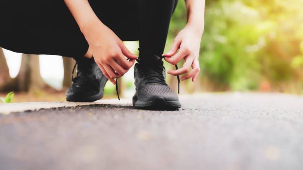 Крупный план женщины, завязывающей шнурки. Азиатская бегунья готовится к пробежке в общественном парке - Фото, изображение