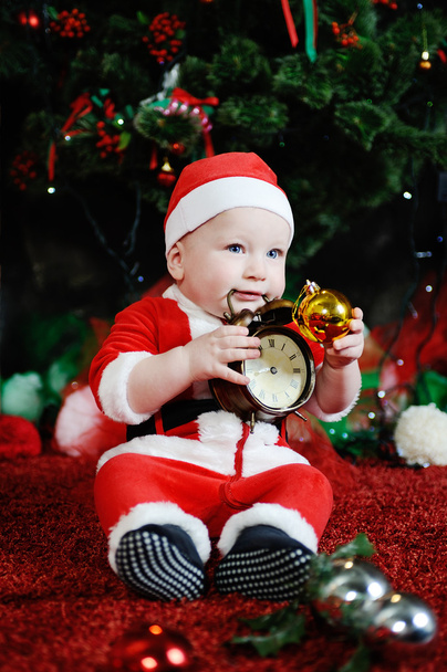 Child dressed as Santa Claus gnawing teeth clock alarm clock. - Фото, изображение