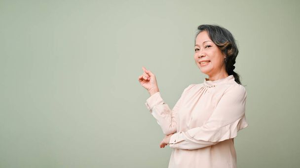Onnellinen ja iloinen 60-luvulla eläkkeellä aasialainen nainen rento vaatteita hymyilee ja seisoo eristetty yli vihreä studio tausta. Kopioi tilaa tekstin esittämistä varten - Valokuva, kuva