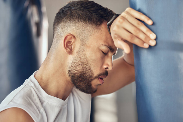 Exhausted boxer resting after workout routine. Tired mma fighter taking a break from exercise routine. Combat fighter leaning on punching bag. Strong athlete relaxing after workout. - Photo, Image