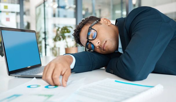 Joven hombre de negocios de raza mixta durmiendo la siesta y trabajando en un portátil en una mesa sola en el trabajo. Un empresario hispano cansado durmiendo trabajando en un escritorio en una oficina. - Foto, imagen