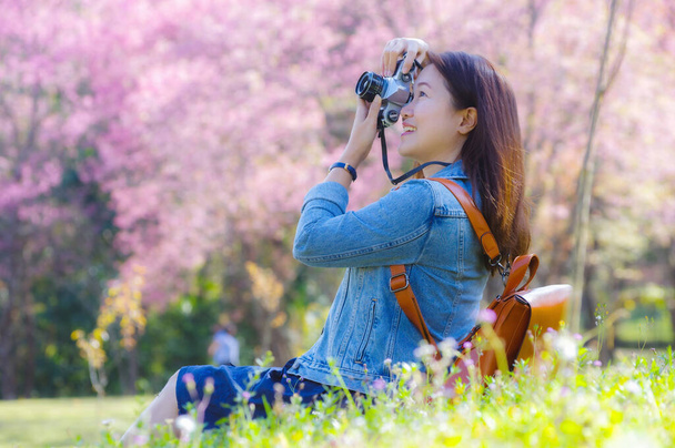 Klasik fotoğraf makinesi kullanan genç, güzel Asyalı bir gezgin. Bahar kiraz çiçeklerinin ortasında gülümseyen bir mutlu fotoğraf çek. Seyahat yaşam tarzı, dünya gezgini, Asya seyahat fikri.. - Fotoğraf, Görsel