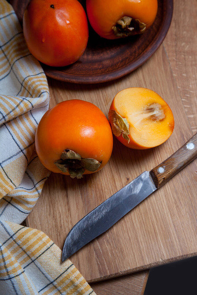 熟したおいしい全体の柿の果物、半分と木の背景にヴィンテージナイフで食べる準備ができてスライスされた果物の構成 - 写真・画像