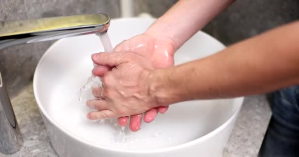 Szoros férfi kézmosás nagy fehér mosogató otthon hotel fürdőszobájában. Férfi napi higiéniai testápolás férfi kezet mos mossa tenyér tisztítja baktériumok coronavirus járvány megelőzése a szállodai szobában - Felvétel, videó