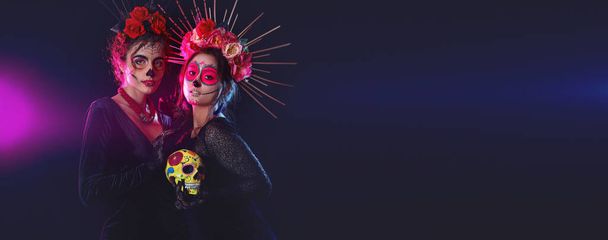 Vrouwen met geschilderde schedels op gezichten tegen donkere achtergrond met ruimte voor tekst. Viering van Mexico 's Dodendag (El Dia de Muertos)) - Foto, afbeelding