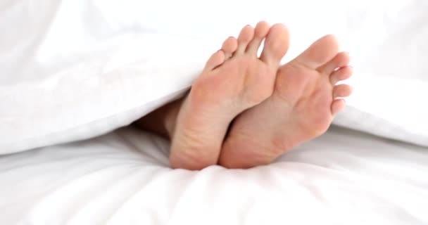 Close-up van vrouwelijke naakte benen in bed. Mooie benen steken onder de deken uit - Video