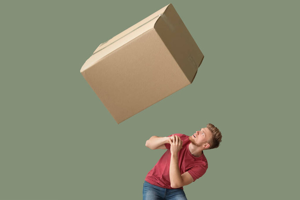 Young man dodging the cardboard box on color background - Fotoğraf, Görsel
