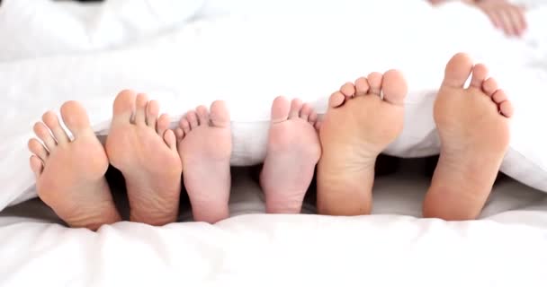 Yatakta yan yana oturan tanınmayan aile bacakları görülüyor. Mutlu aile sabahları evde ya da otelde uyur. - Video, Çekim