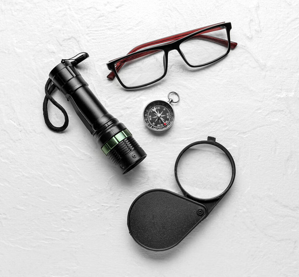 Eyeglasses, compass, magnifier and flashlight on light background - Photo, Image