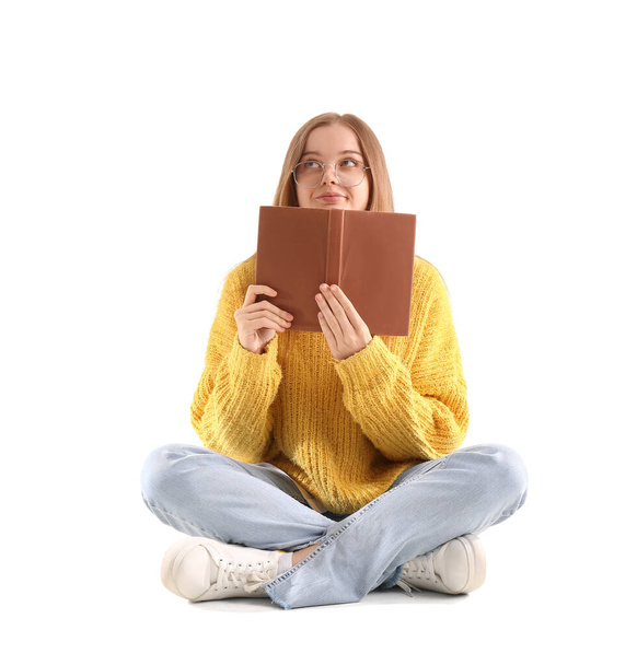 Giovane donna in maglione giallo con libro seduta su sfondo bianco - Foto, immagini