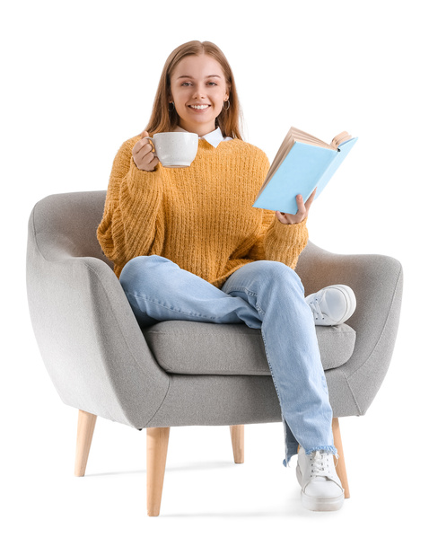 Mujer joven con libro y taza de cacao caliente sentada en sillón sobre fondo blanco - Foto, imagen