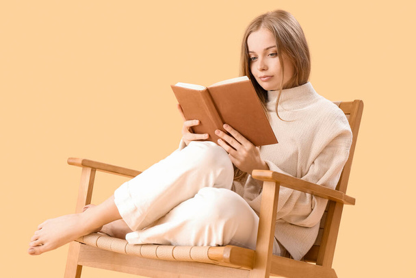 Молодая женщина читает книгу в кресле на бежевом фоне - Фото, изображение